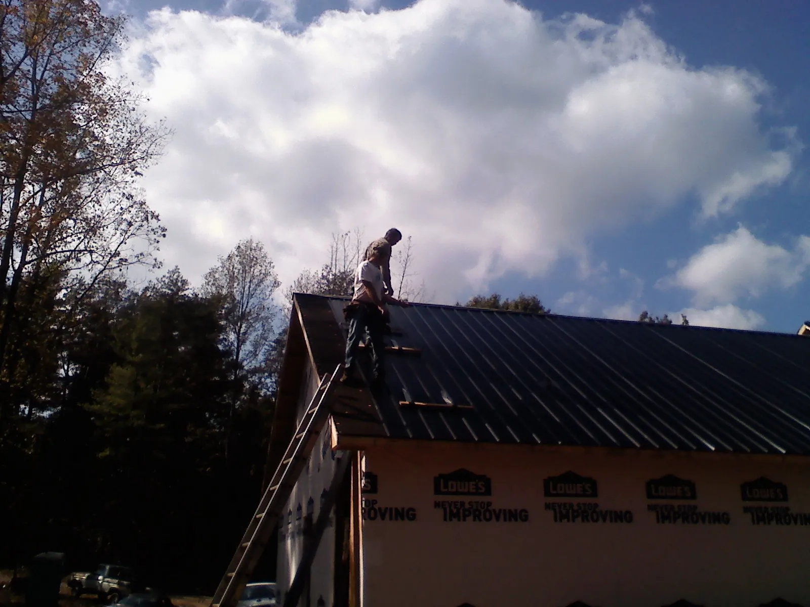 Roofer fastening dark metal panels high against a cloudy sky, from a Roof Inspection job in Brookfield